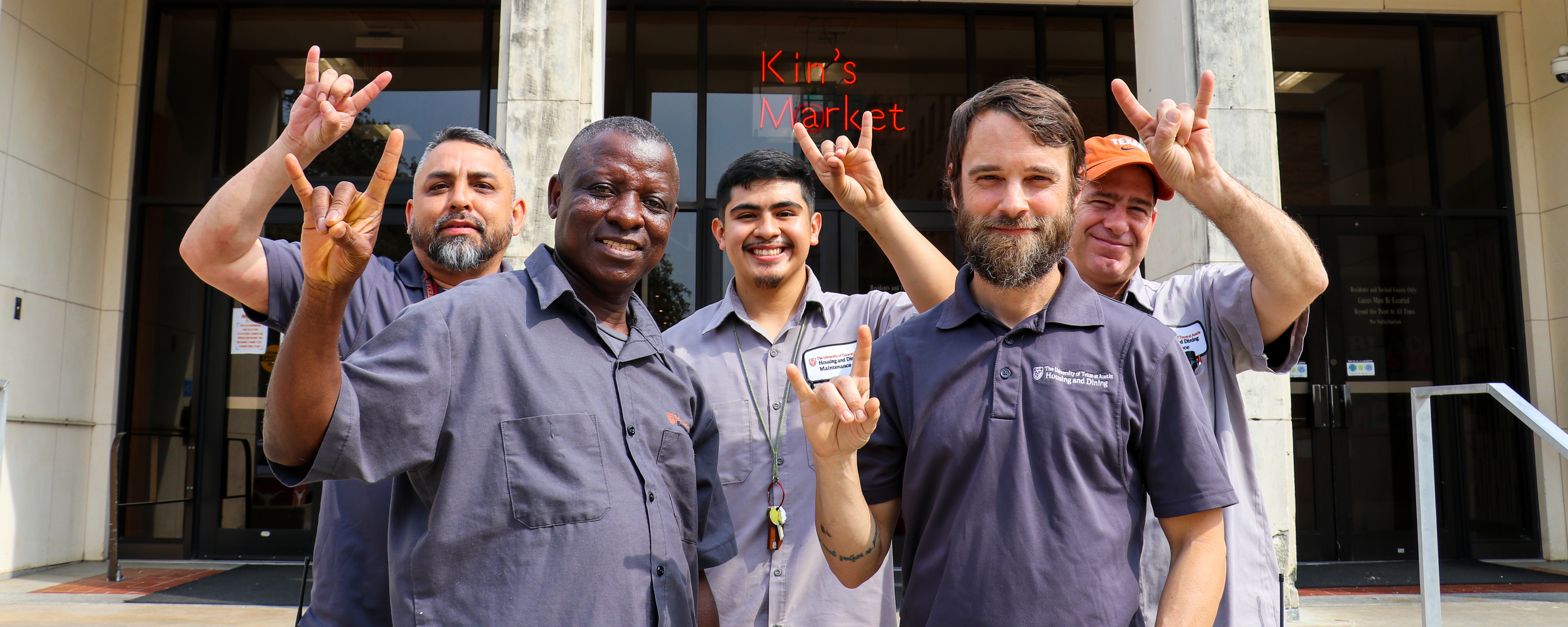 Five UHD employees outside smiling and holding up the UT Longhorns symbol with their hands.
