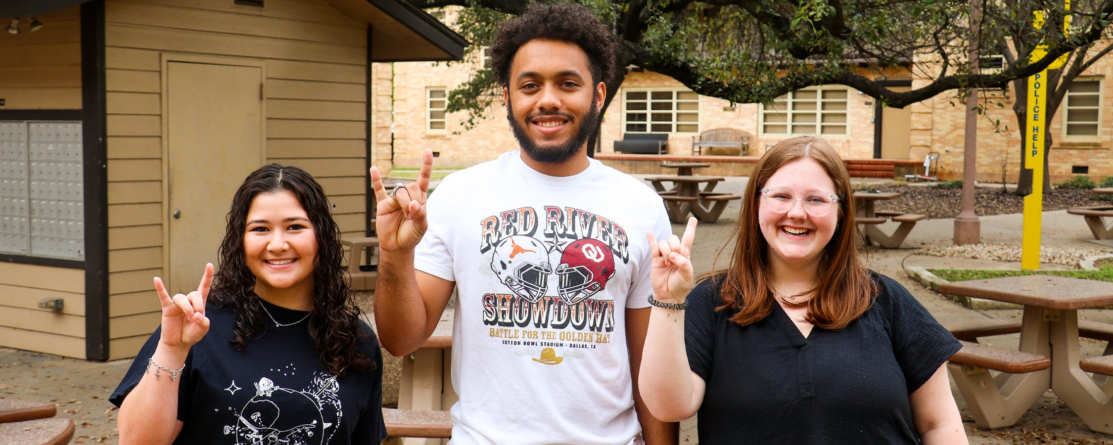 Three students smiling outside while posing with University of Texas hand symbol.