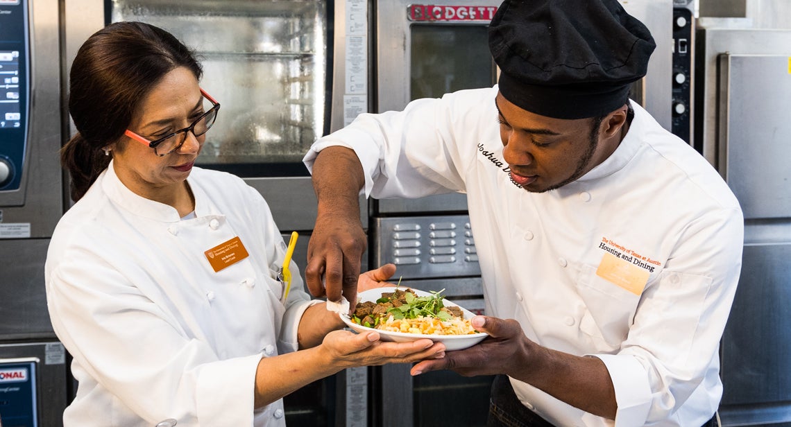 A UHD chef wipes a plate of food while another holds it inside the Jester kitchen.