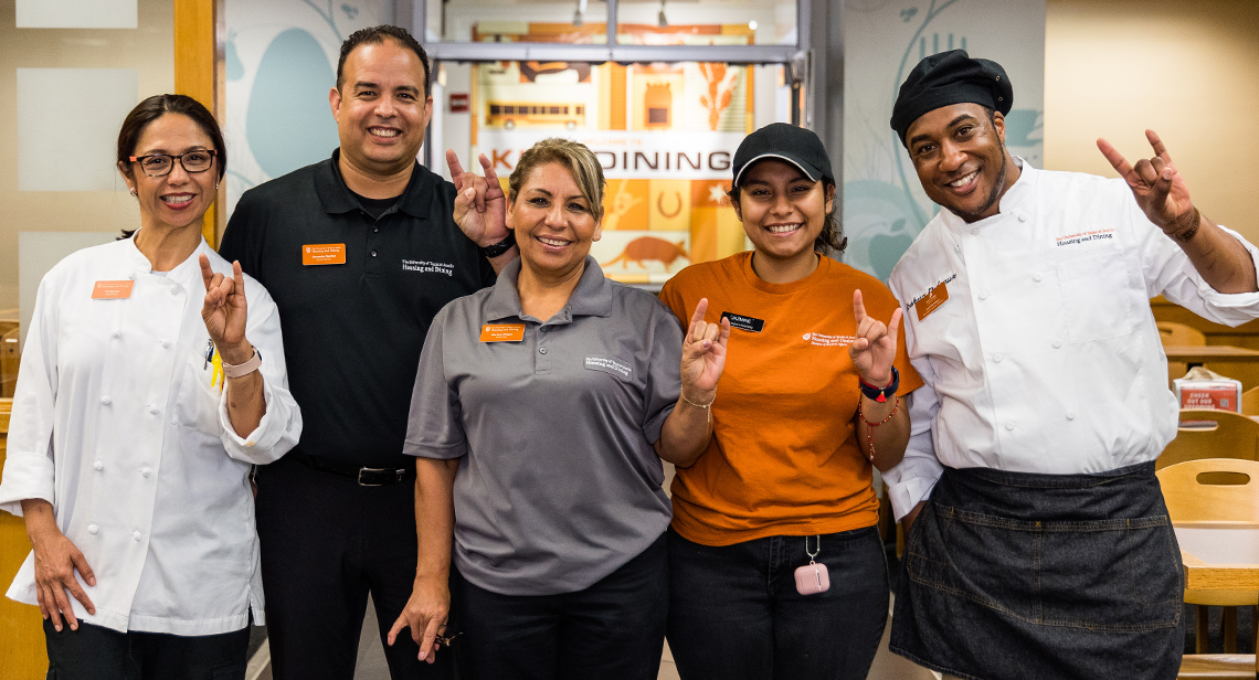 Five UHD Dining staff members smile with Hook ‘em hand signs inside Kins Dining.