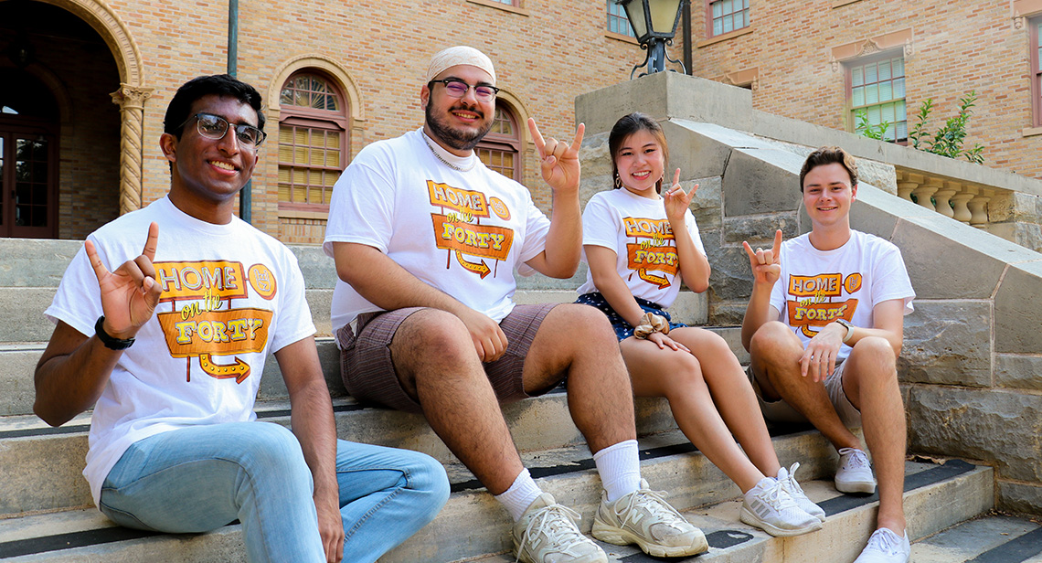 Four UT students pose in Home on the Forty shirts outside Littlefield Hall