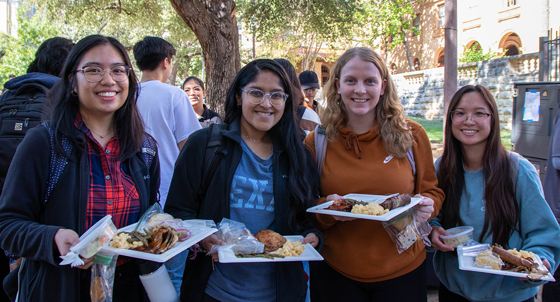 Four UT students pose with plates of food at the fall 2022 Northside Bash