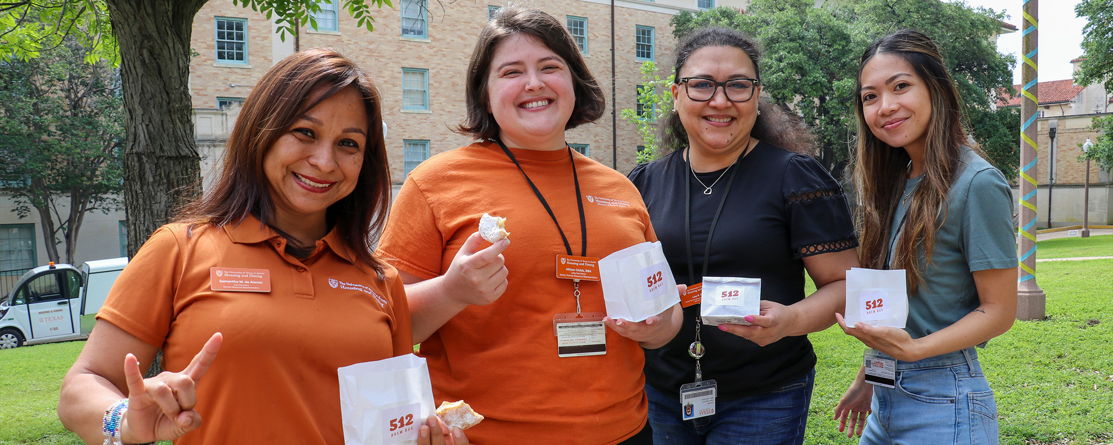 Four UHD staff members pose with bags of beignets in the Honors Quad courtyard