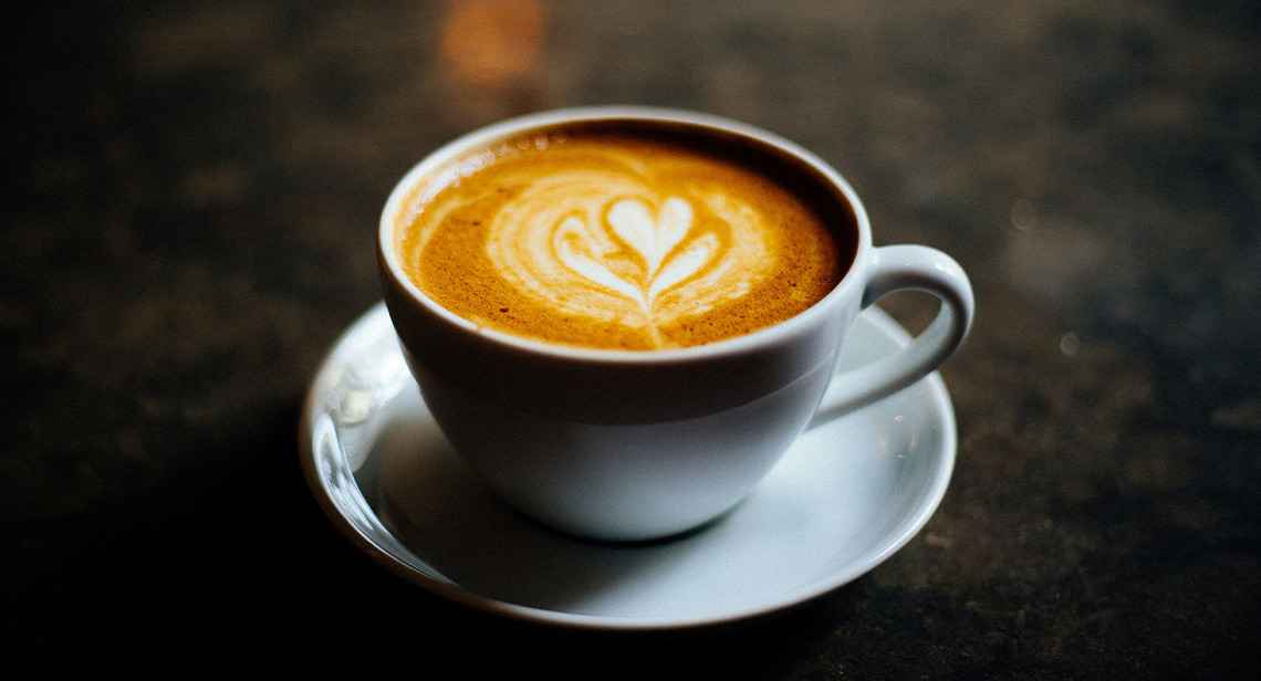 A mug displaying latte art and saucer on a table.