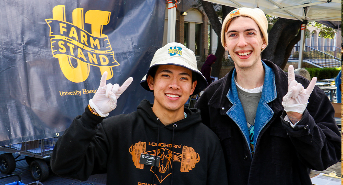 Two students pose together in front of a UT Farm Stand sign