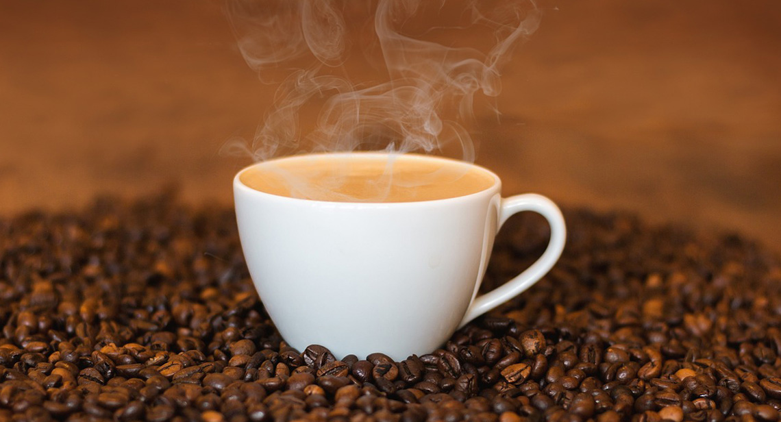 A steaming cup of coffee surrounded by coffee beans.