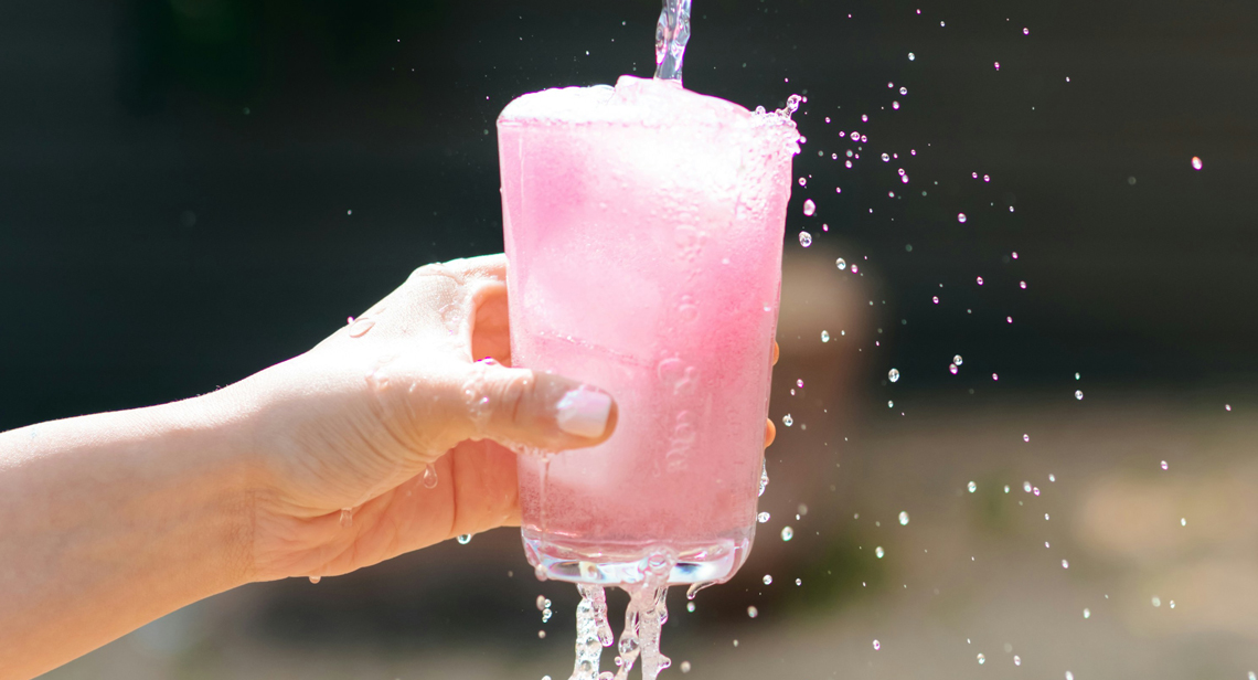 A hand holding a pink fizzy drink