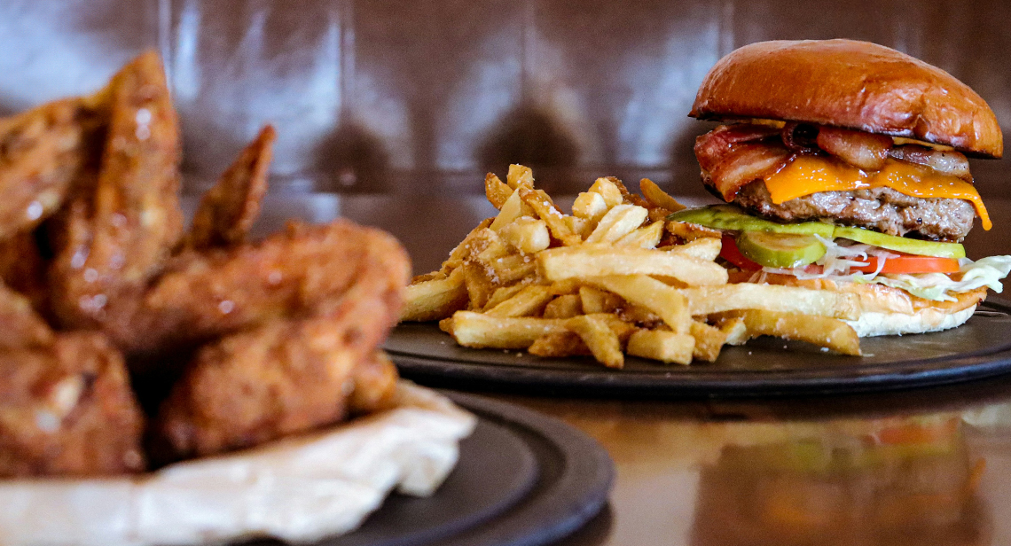 Plates of wings, a burger and fries on a table. 