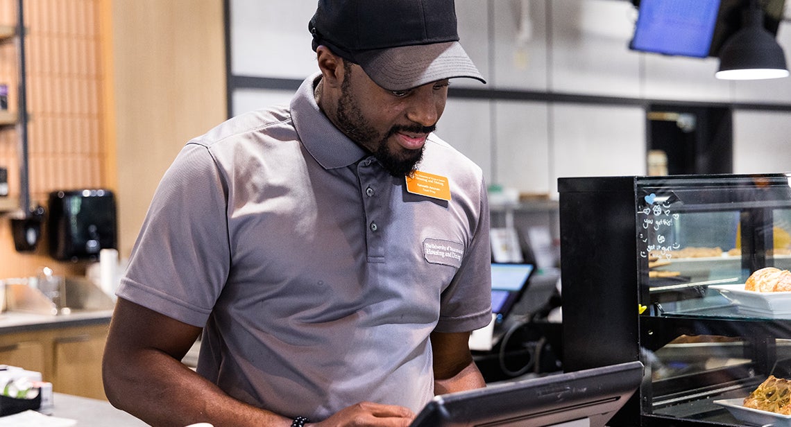 A UHD student staff member works at a cash register at Littlefield Patio Cafe.