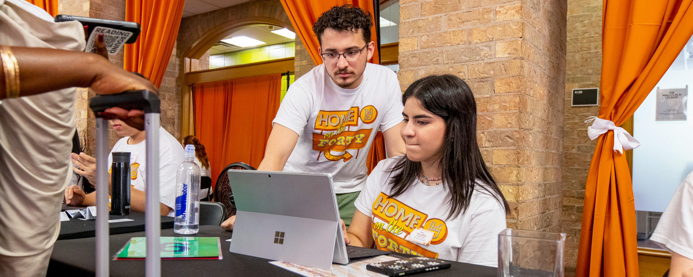 Two UT students check guests in on a tablet at New Student Orientation