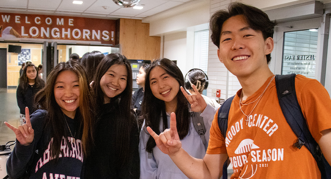 Four UT students pose together with Hook 'em hand signs inside Jester East Hall