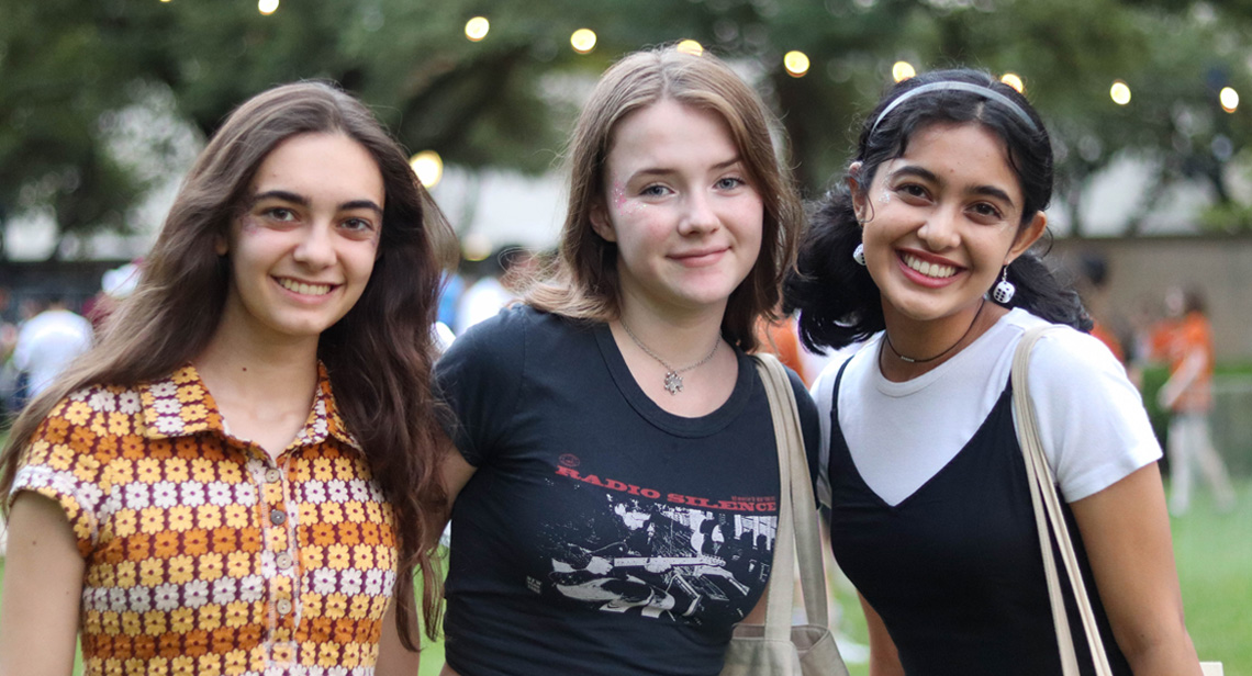 Three students pose with smiles outside