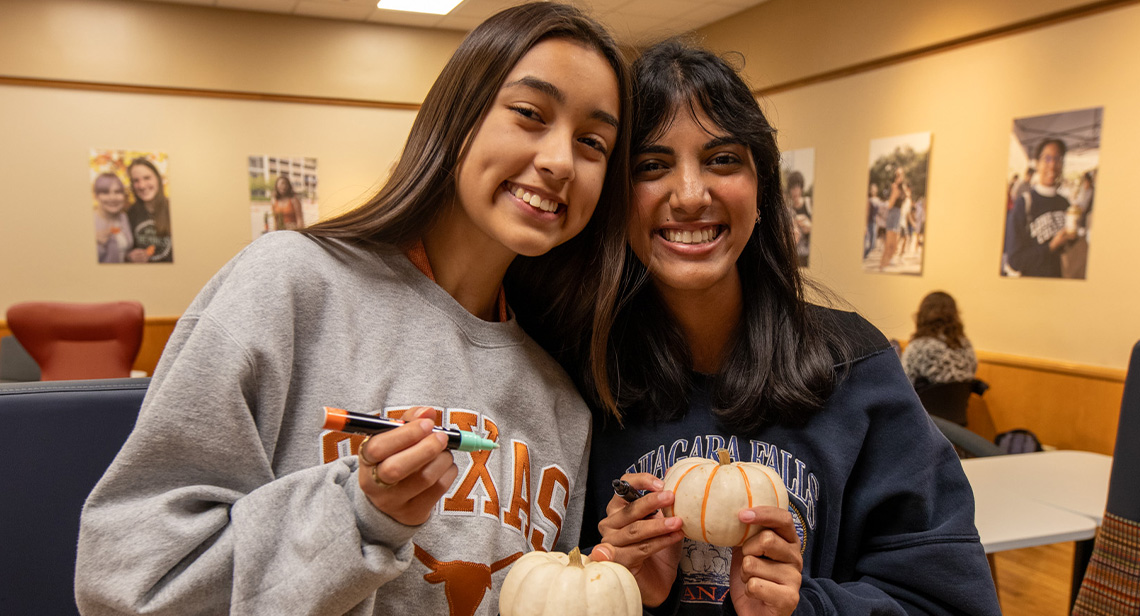 Two UT students pose together while holding pumpkins at the Halloween Extravaganza event