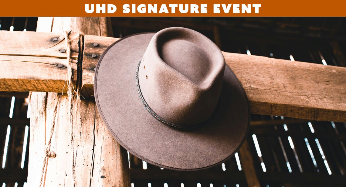 A cowboy hat hangs on a wooden post with text on a banner reading, “UHD Signature Event” on the top