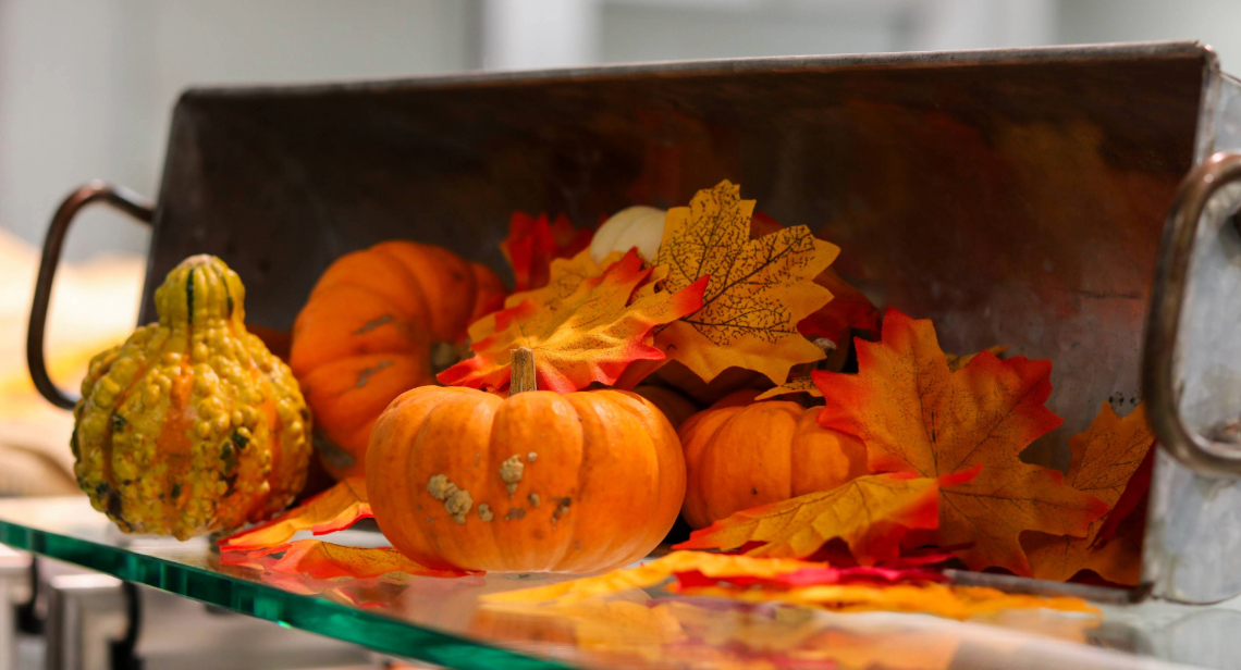  A decorative display featuring a basket, small pumpkins and autumn leaves.