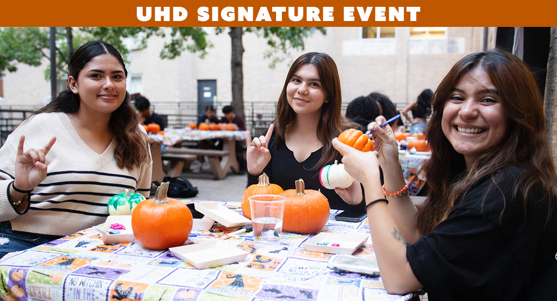  Three UT students paint pumpkins at the Hall-oween Campus Crawl event at Jester Plaza with text on a graphic banner reading, "UHD Signature Event" on the top.