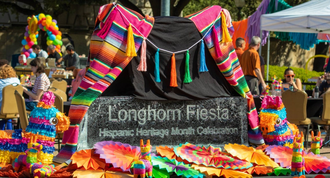 Colorful decorations, including piñatas and sarapes, surround an ice sculpture reading, 'Longhorn Fiesta Hispanic Heritage Month Celebration' at the Longhorn Fiesta event on the Main Mall.