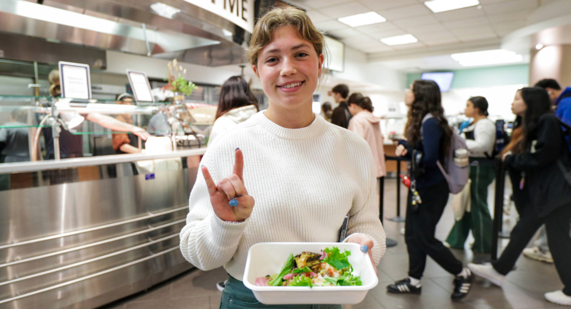 Student posing with a Hook ‘em hand sign inside of Kins Dining