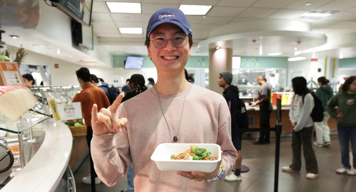 Student posing with a Hook ‘em hand sign inside of Kins Dining