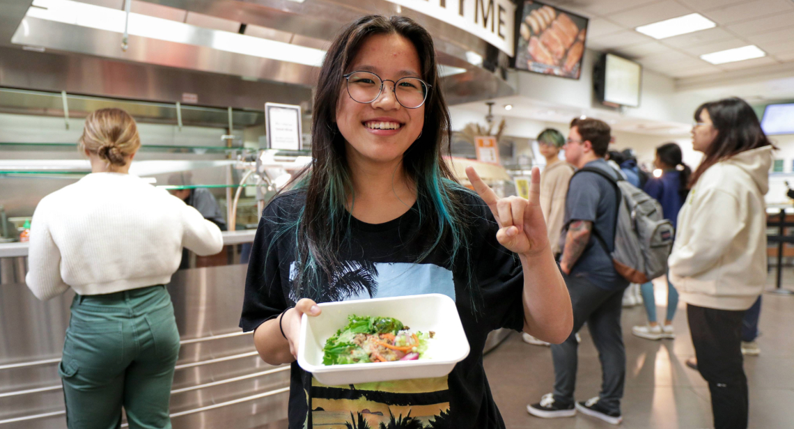 Student posing with a Hook ‘em hand sign inside of Kins Dining