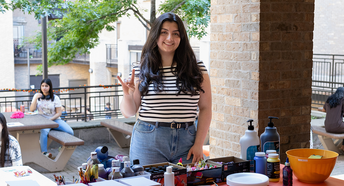 A UT student makes the Hook ‘em hand sign while standing behind a table with craft supplies at Jester Plaza.