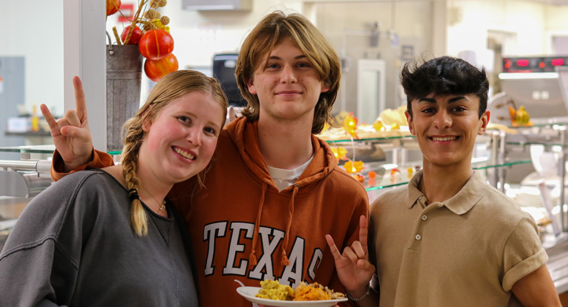 UT students pose and make the Hook ‘em hand sign while holding plates of food at  Kins Dining. 