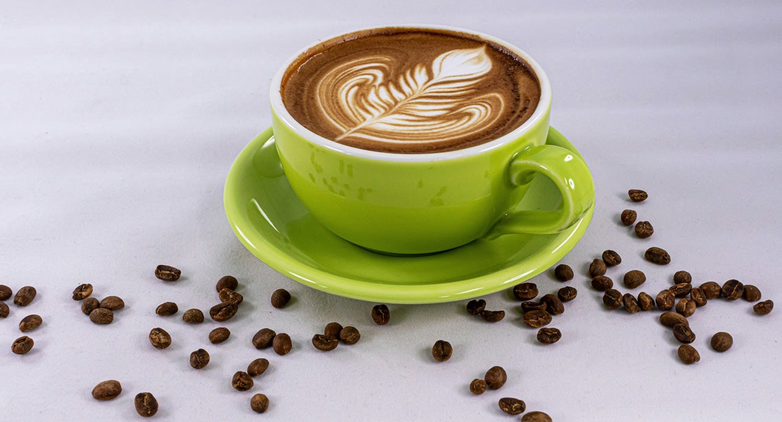 A cup of coffee on a table surrounded by coffee beans