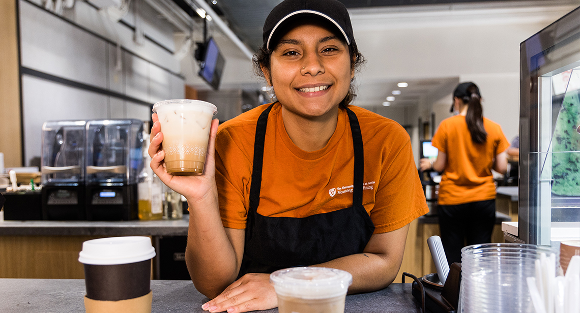 UHD student barista holds an iced coffee drink at Littlefield Patio Cafe