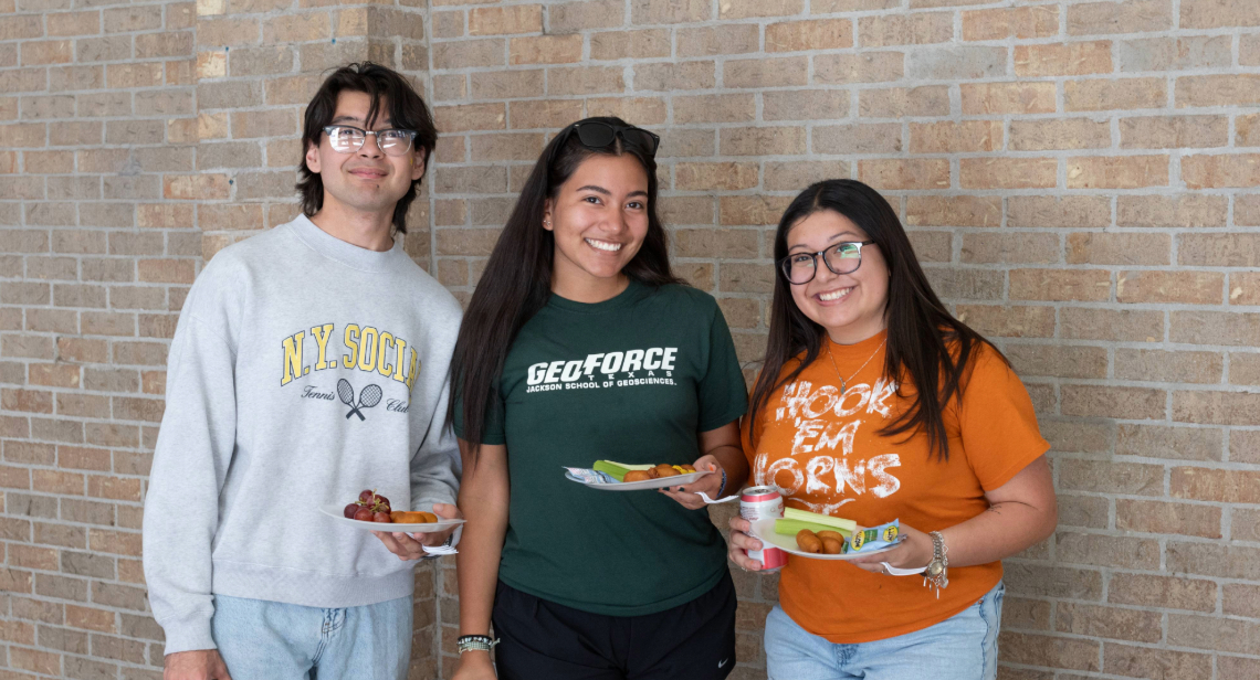 Three UT students smiling with plates of food outside Jester