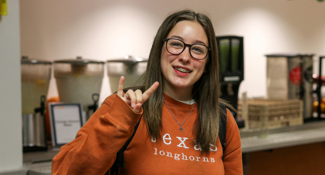 Student posing with Hook ‘em hand sign inside of Kins Dining