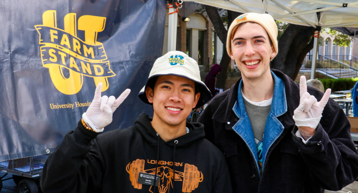 Two UT Farm Stand student employees posing with Hook ‘em hand signs on Jester Corner