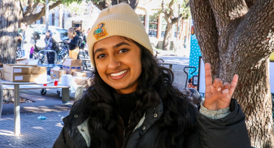 Student with UT Farm Stand beanie posing with a Hook em hand sign on Jester Corner