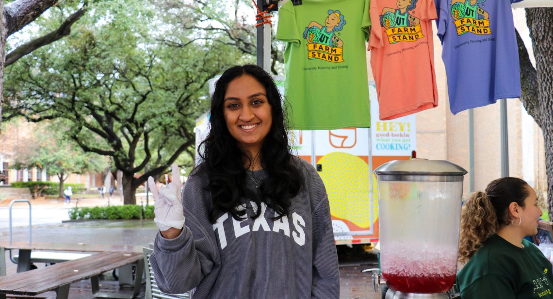 UT Farm Stand student employee posing with a Hook ‘em hand sign on Jester Corner