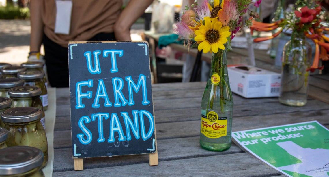 UT Farm Stand sign on a table with jars of pickles and a glass bottle with flowers