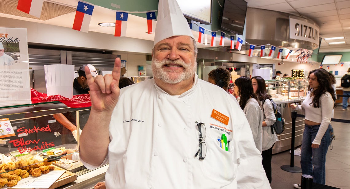 A UT staff member poses while making the Hook ‘em hand sign in Kins Dining