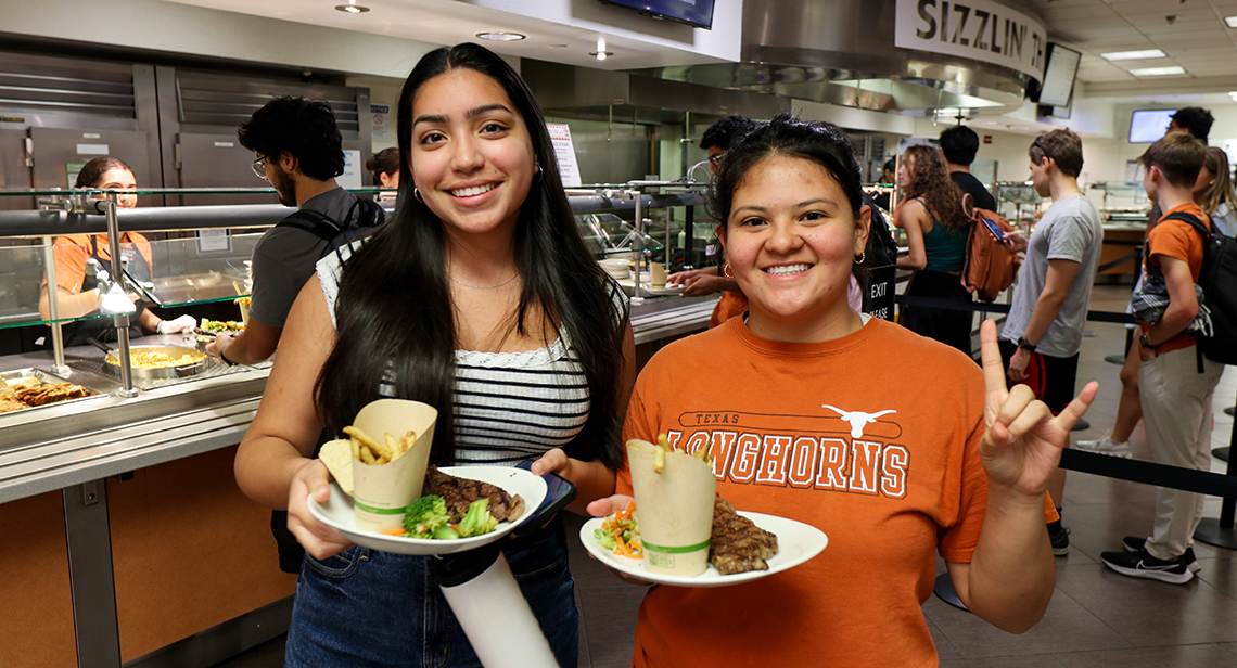 Two UT students pose together while holding plates of food in Kins Dining.