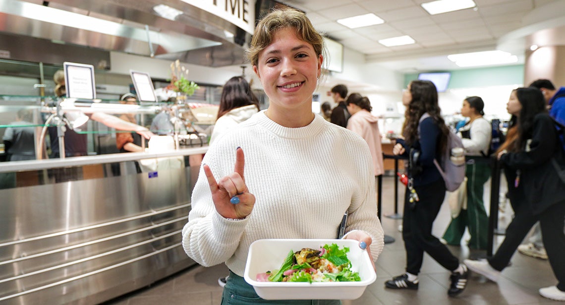 A UT student makes the Hook ‘em hand sign while holding a bowl of food