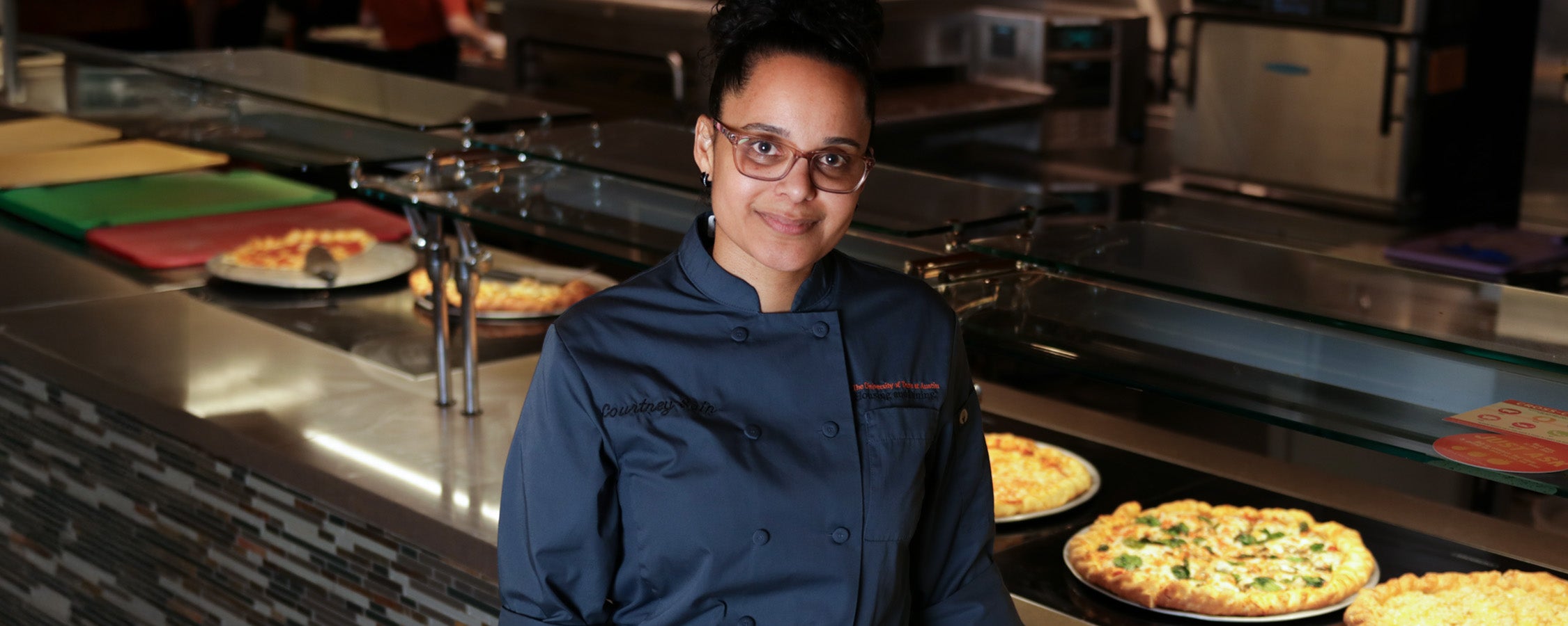 A UT staff member stands in front of a pizza buffet in J2 Dining