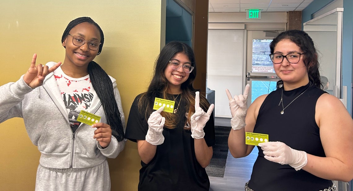 Three UT students posing with a Hook ‘em hand sign and their UHD dietitian event stamp card