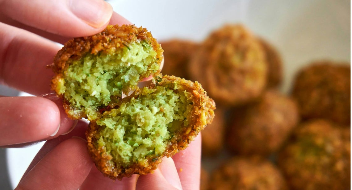 A person’s hands holding a baked falafel snack