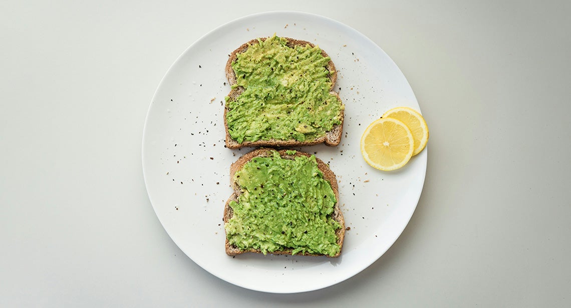 Two pieces of avocado toast and lemon slices on a plate