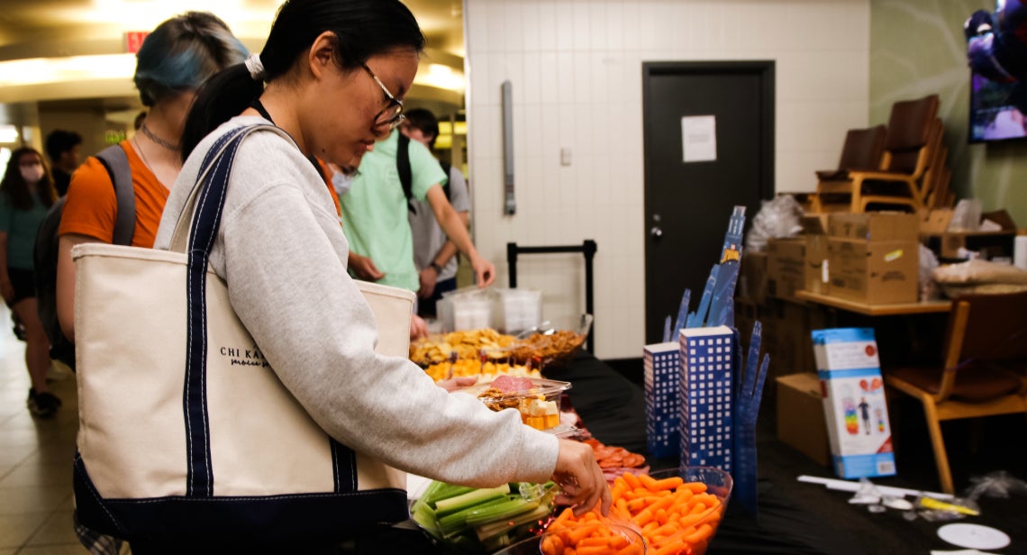 A UT student making a plate of snacks from an assortment of cheeses, crackers and pretzels, meats and vegetables