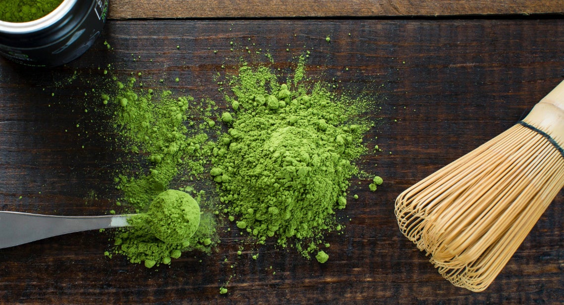 A teaspoon of matcha green powder alongside a traditional bamboo whisk