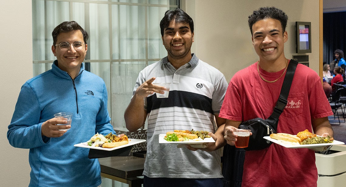 Three UT students pose together while holding plates of food in San Jacinto Hall