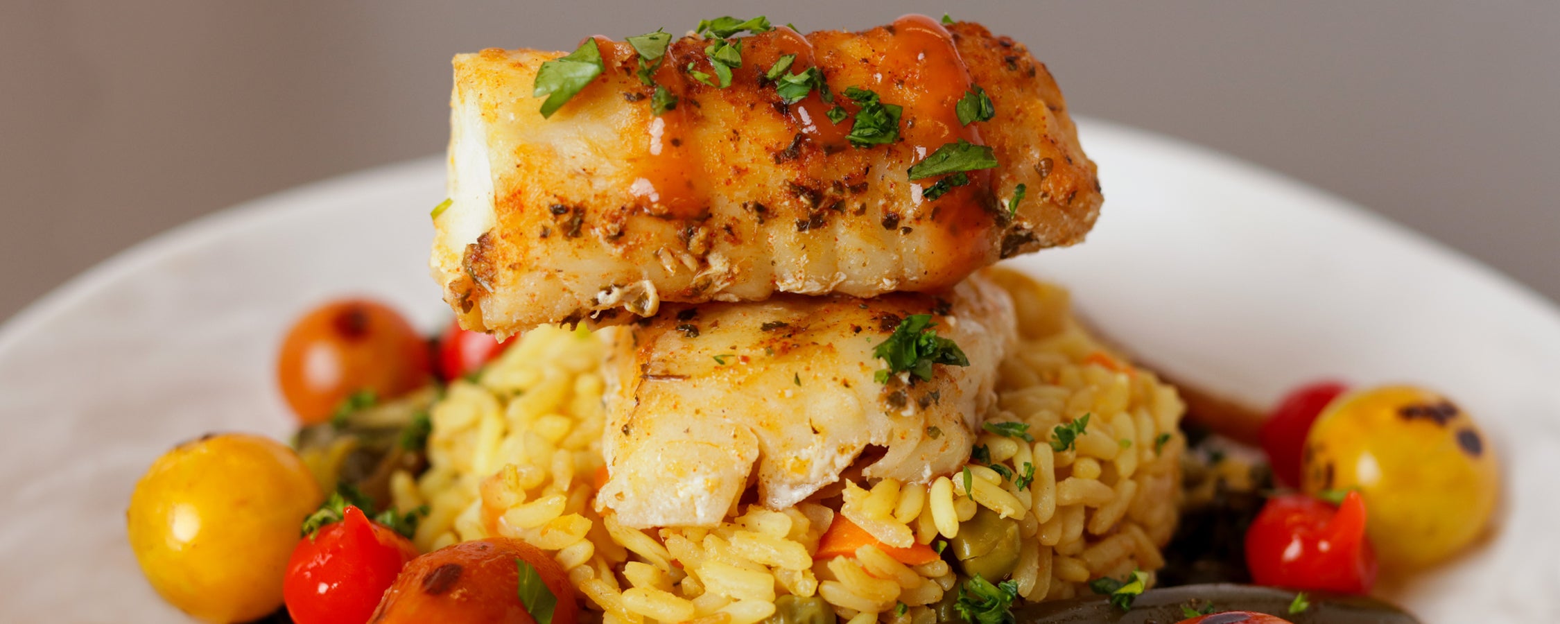 A prepared dish with fish, rice and various vegetables topped with herbs and sauce