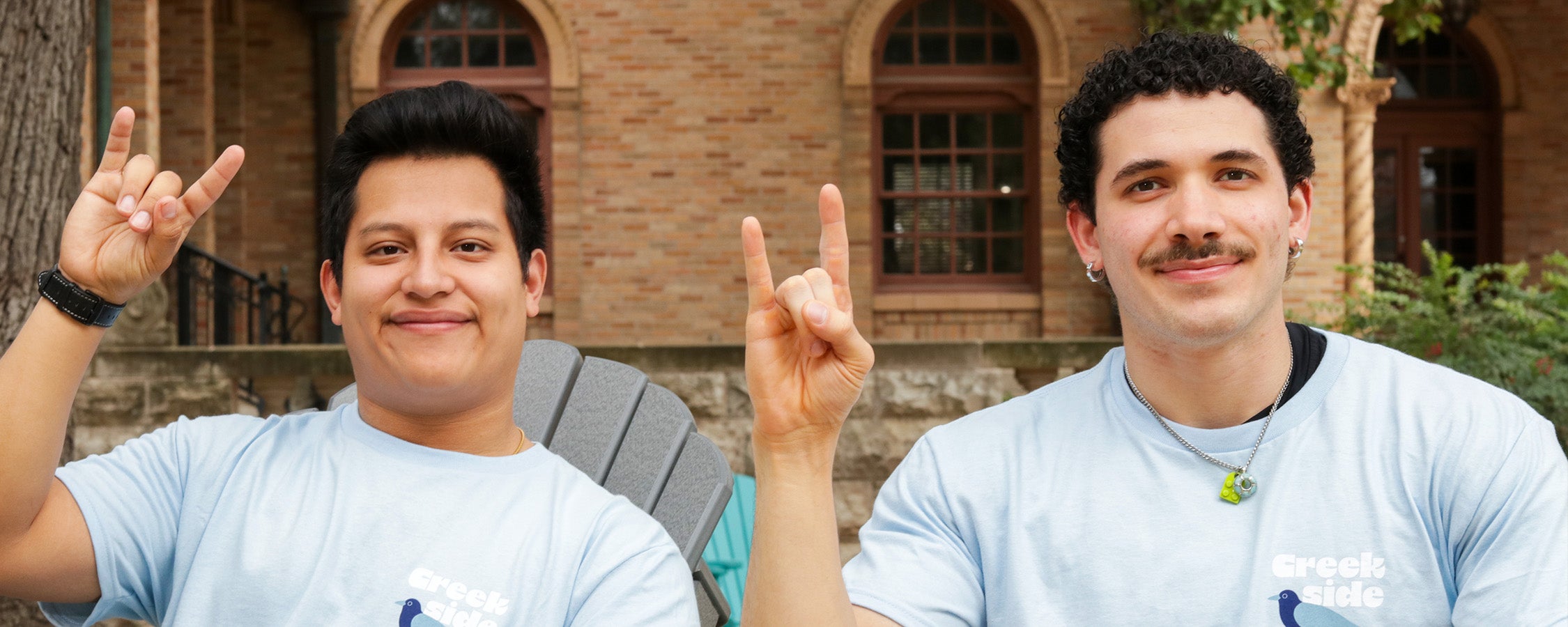 Two Resident Assistants make the Hook ‘Em hand sign in front of Littlefield Hall.
