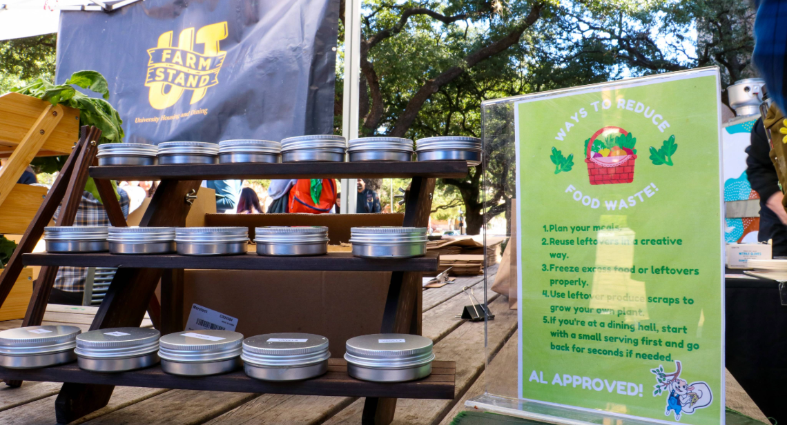 A table with reusable tin cans and a sign about reducing food waste at the UT Farm Stand Market