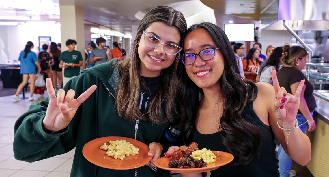Two UT students posing with plates of food inside a dining hall