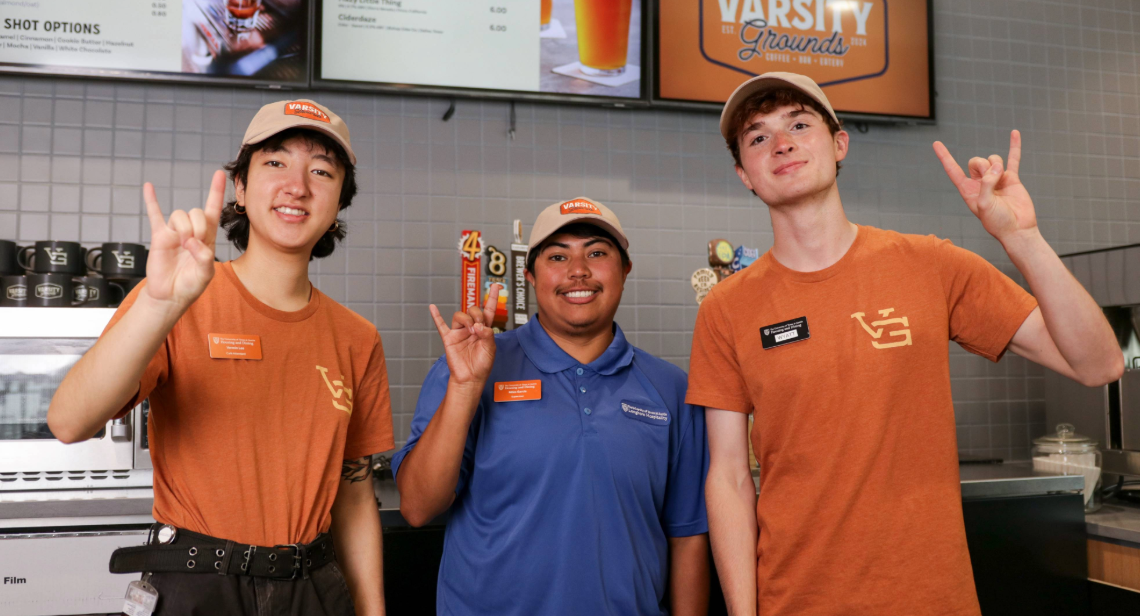 Three UT student dining workers posing with a hook ‘em hand sign at Varsity Grounds.