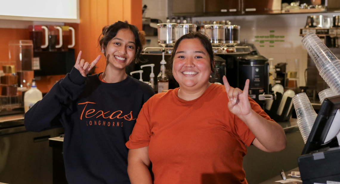 Two UT student dining workers posing with a hook ‘em hand sign at Jester Java.